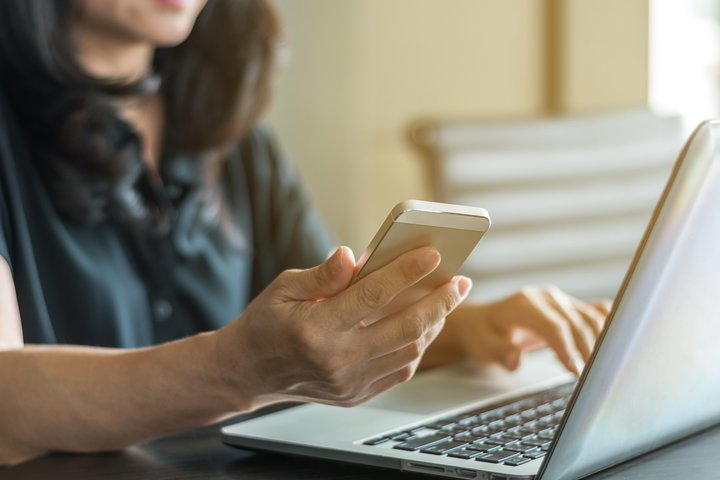 Moteris dirbanti su kompiuteriu ir mobiliuoju telefonu
