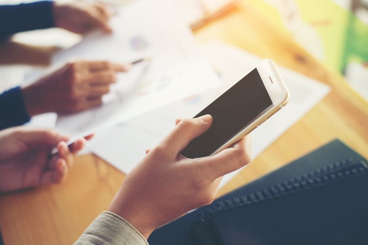 Du žmonės pasirašo dokumentus ir naudojasi mobiliuoju telefonu